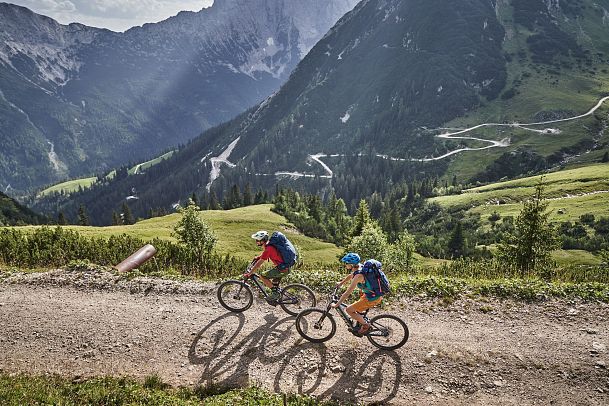 Zwei Mountainbiker auf einem Schotterweg in den Bergen.