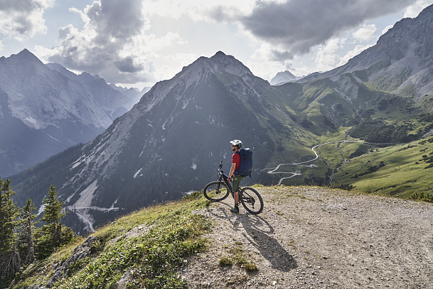 Mountainbiker auf Bergpfad mit Alpenblick. Dramatische Wolken am Himmel.