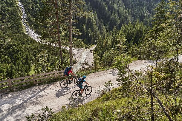 Zwei Radfahrer auf einem Waldweg in der Region Seefeld. Alpenlandschaft, Bäume, steiniger Pfad. Radfahren, Naturerlebnis.