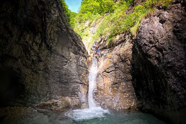 Wasserfall fließt zwischen steilen Felsen in einen kleinen Pool.