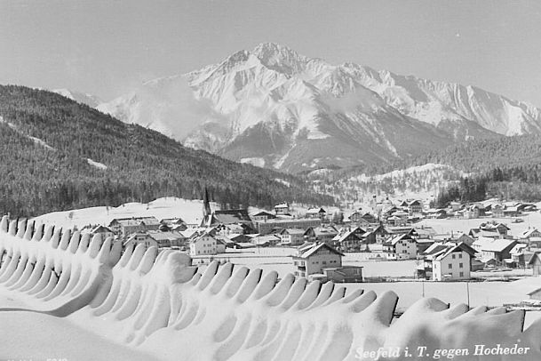 Winterliche Landschaft mit schneebedeckten Bergen und einem Dorf im Vordergrund.