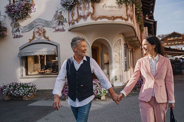 Lächelndes Paar spaziert durch blumengeschmückte Straße mit traditioneller Architektur.