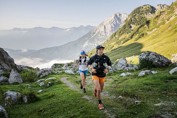 Zwei Läufer in einer grünen Berglandschaft beim Trailrunning, umgeben von Bergen.
