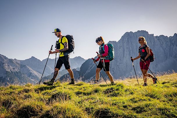 Drei Wanderer mit Rucksäcken und Stöcken in den Alpen. Im Hintergrund Alpenpanorama. Keyword: Wandern, Alpen.