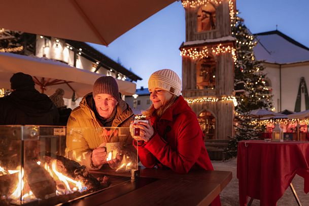 Weihnachtsmarkt Seefeld_Paar steht am Feuertisch_Mann und Frau schauen ins Feuer