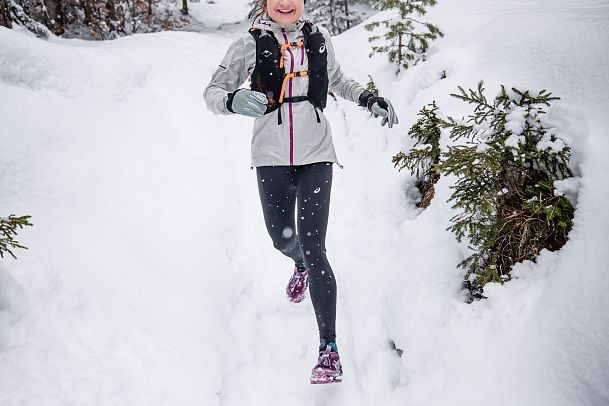 Wintertrailrunning in der Region Seefeld (abseits der Wege) - Lachende Läuferin im Schnee mit Wald im Hintergrund