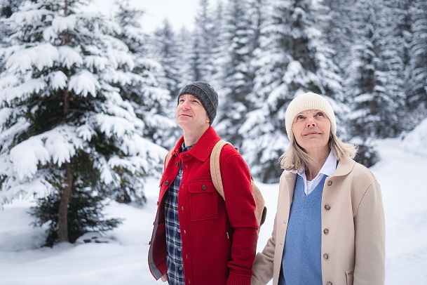 Winterwandern im Wildmoos_Paar läuft durch verschneiten Wald_Frau blickt in die Bäume