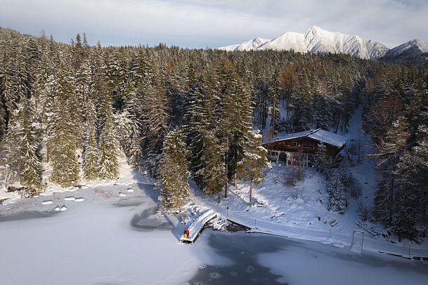 Winterwandern Paar Möserer See Drohnenaufnahme Paar steht am Steg mit Möserer Seestube und Reither Spitze im Hintergrund (1)