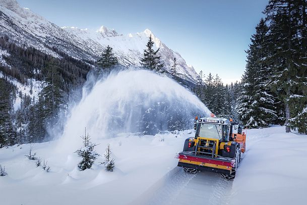 Ein Schneepflug räumt die verschneite Straße in der Region Seefeld, umgeben von verschneiten Bäumen.
