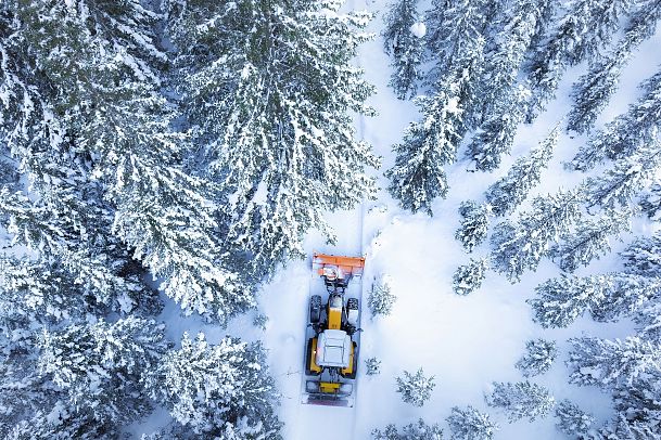 Schneepflug fährt durch verschneiten Wald, umgeben von schneebedeckten Bäumen. Winterlandschaft.