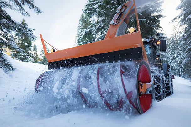 Ein Schneepflug räumt einen verschneiten Waldweg frei. Schneeräumen im Winterwald in der Region Seefeld.