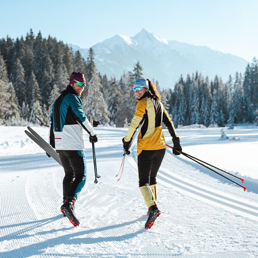 Zwei Langläufer auf einer präparierten Spur in der Region Seefeld, umgeben von verschneiten Bäumen und Bergen.