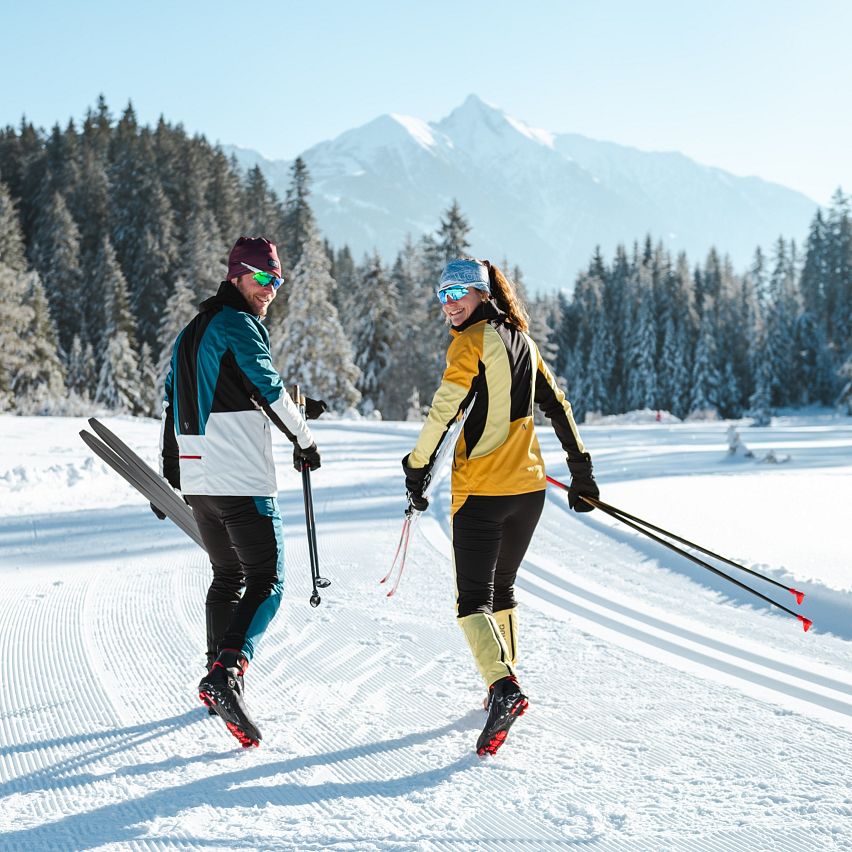 Zwei Langläufer auf einer präparierten Spur in der Region Seefeld, umgeben von verschneiten Bäumen und Bergen.