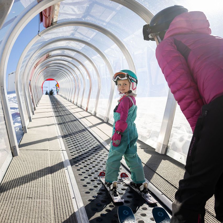 Ein Kind mit Skiausrüstung wartet in einem Förderband-Tunnel auf dem Weg zum Skif in der Region Seefeld.