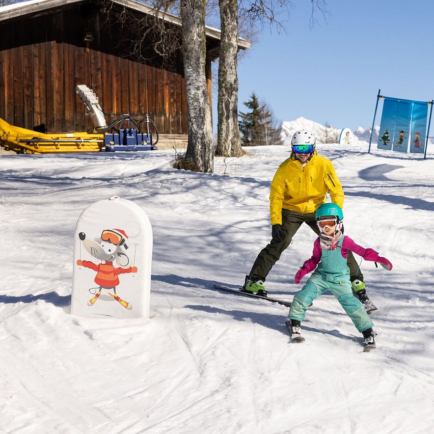 Ein Erwachsener und ein Kind skifahren auf einem verschneiten Hang.
