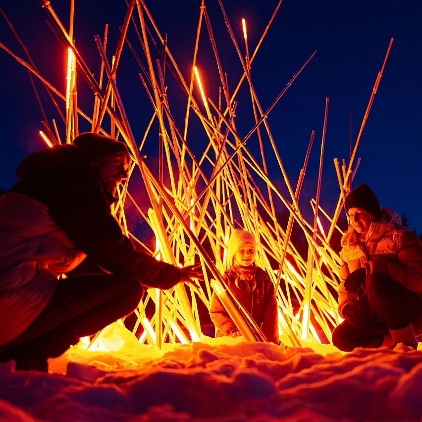 Vier Personen sitzen im Schnee mit leuchtenden Stäben, die eine warme Atmosphäre schaffen. Winterabend in der Region Seefeld.
