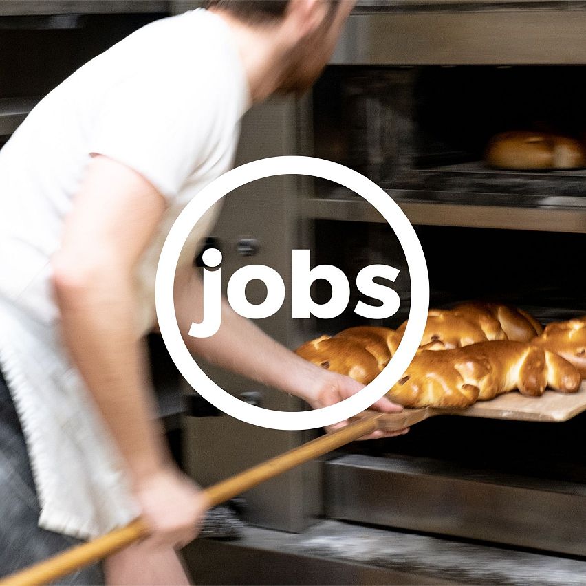 A baker placing bread in an oven with a wooden paddle.