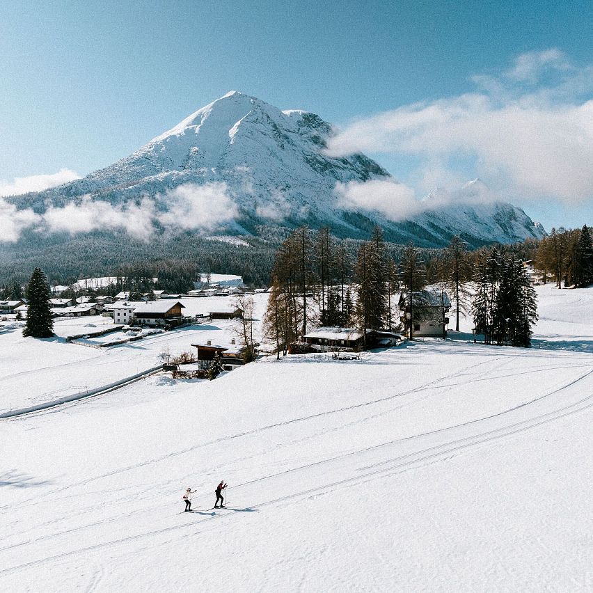 Zwei Langläufer in der Region Seefeld, umgeben von verschneiten Bergen und Wald.