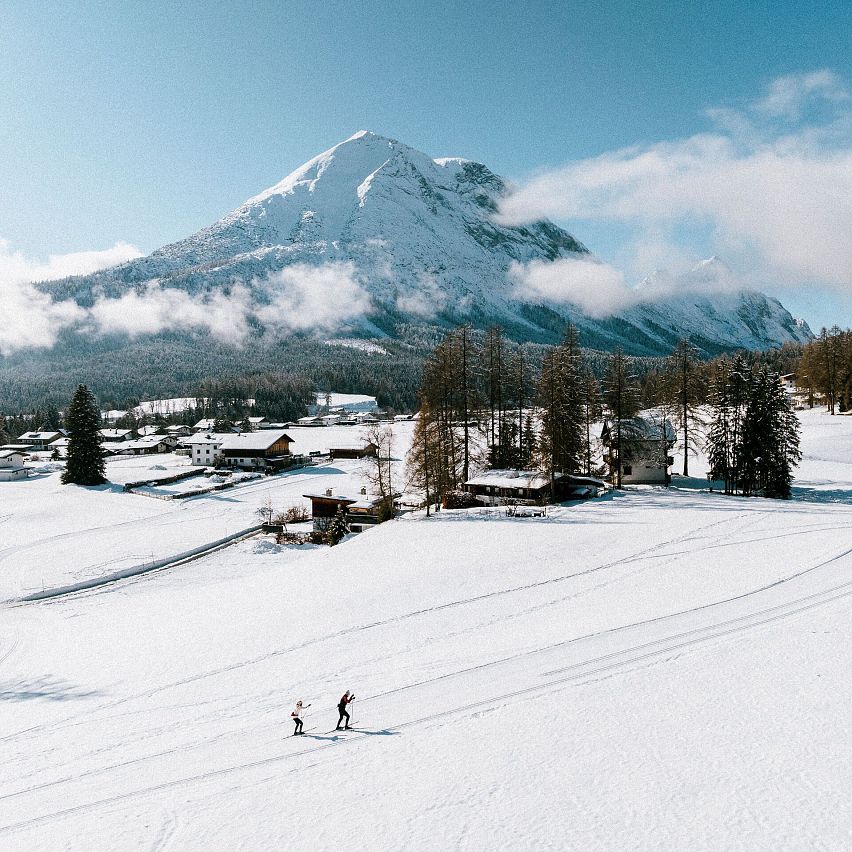 Zwei Langläufer in der Region Seefeld, umgeben von verschneiten Bergen und Wald.
