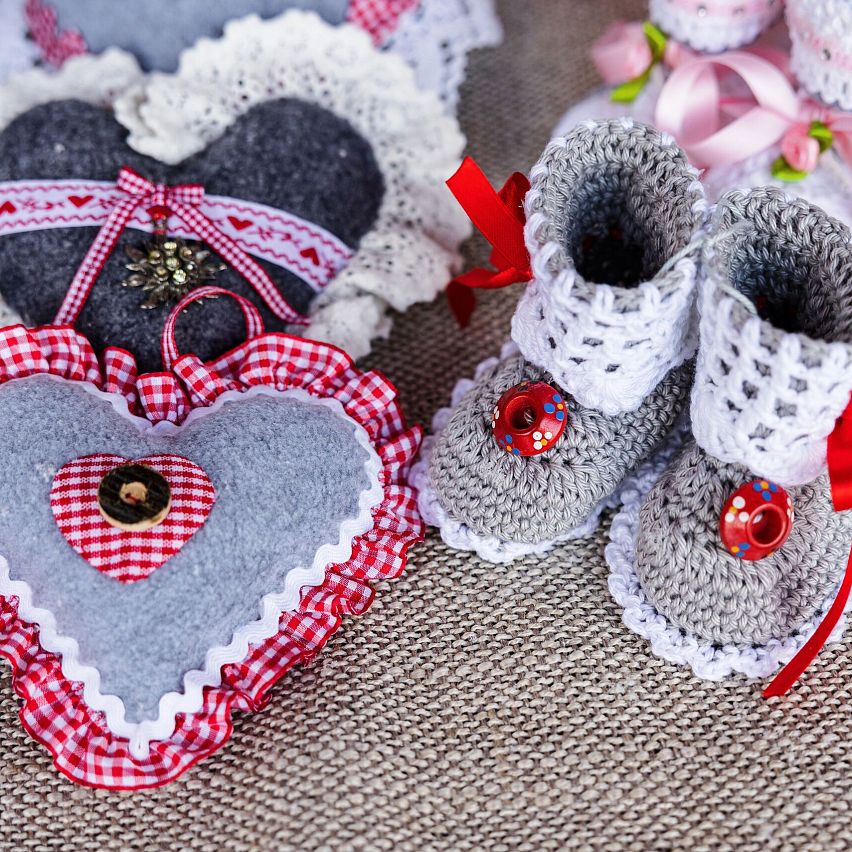 Gestrickte Babyschuhe und gehäkelte Herzen auf Stoffuntergrund. Ideal für Handarbeits- und Dekorationsliebhaber.
