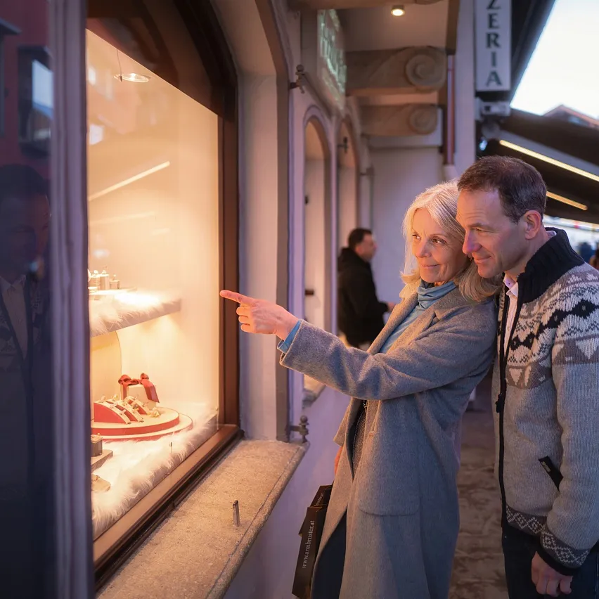 Ein älteres Paar betrachtet gemeinsam ein festlich dekoriertes Schaufenster in einer belebten Straße.