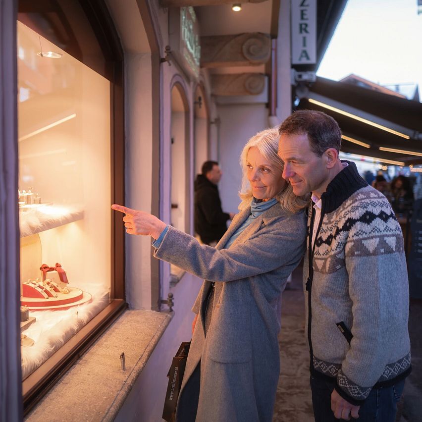 Ein älteres Paar betrachtet gemeinsam ein festlich dekoriertes Schaufenster in einer belebten Straße.