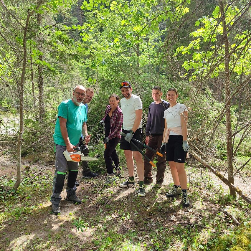Sechs Personen in einem Wald mit Gartenwerkzeugen, umgeben von Bäumen.