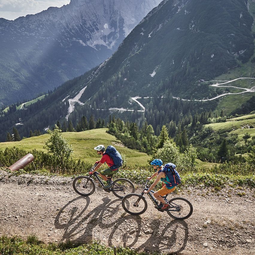 Zwei Mountainbiker auf einem Schotterweg in alpiner Landschaft. Berge im Hintergrund. Ideal für Mountainbike-Touren.