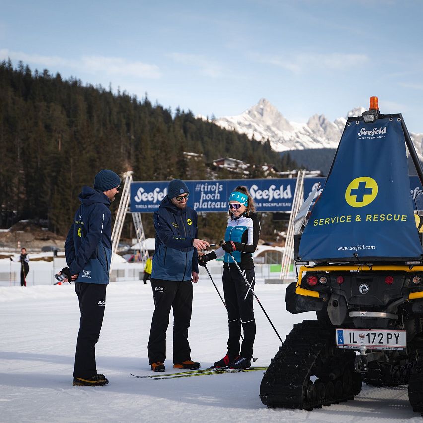 Ski patrol and a skier talking beside a rescue vehicle in a snowy area.