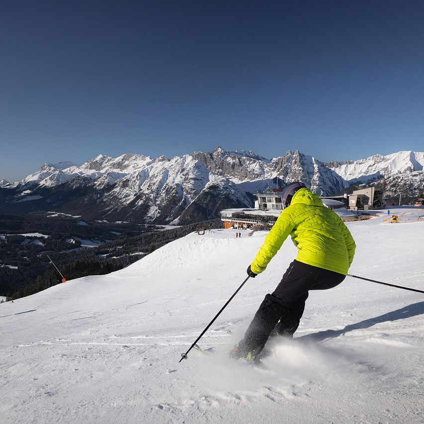 Skifahrer in gelber Jacke auf Piste in der Region Seefeld, umgeben von schneebedeckten Bergen.