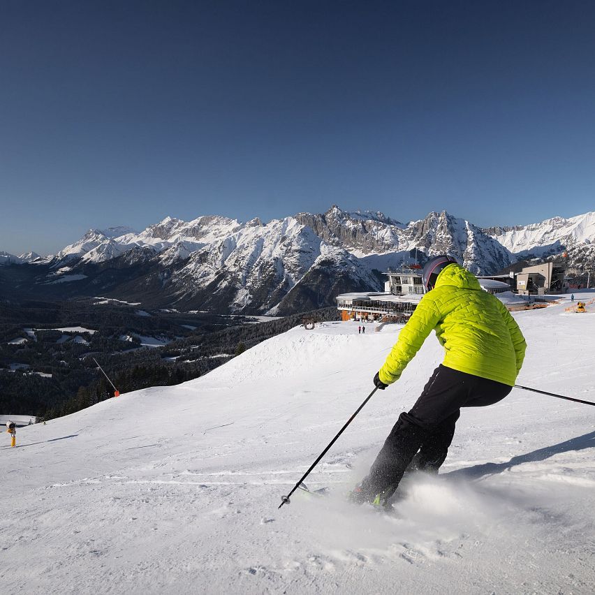 Skifahrer in gelber Jacke auf Piste in der Region Seefeld, umgeben von schneebedeckten Bergen.