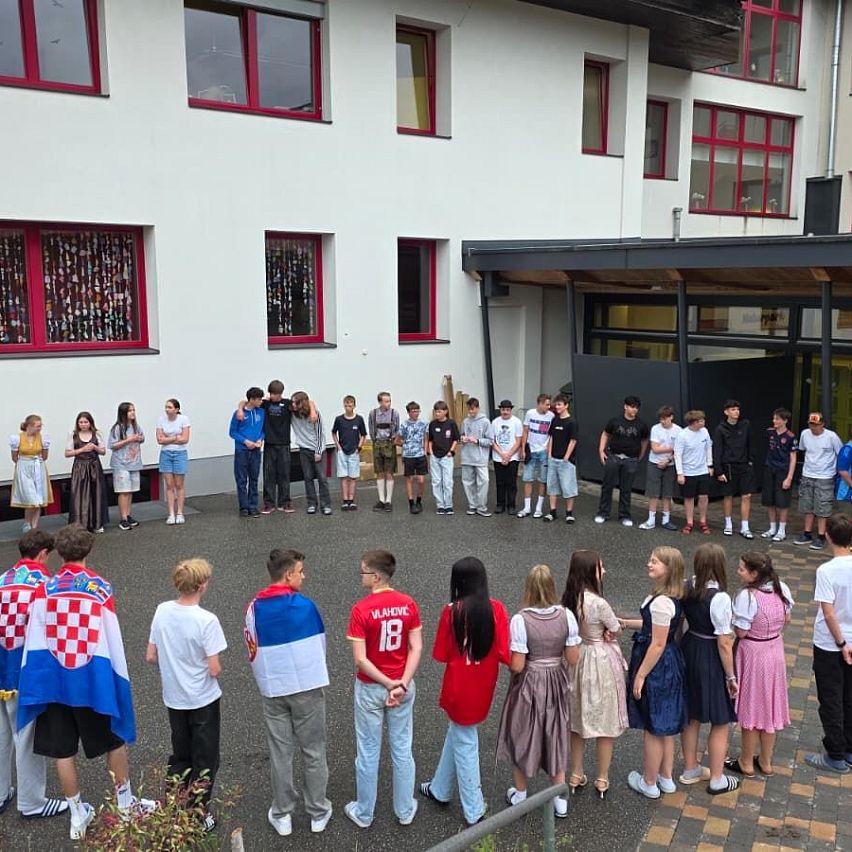 Schüler versammeln sich zu einer Veranstaltung in einem Innenhof vor einem Schulgebäude.
