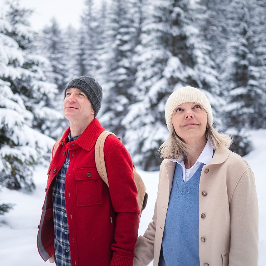 A man and woman explore the snowy forest in the Region Seefeld, admiring the winter scenery amidst tall, snow-covered trees.