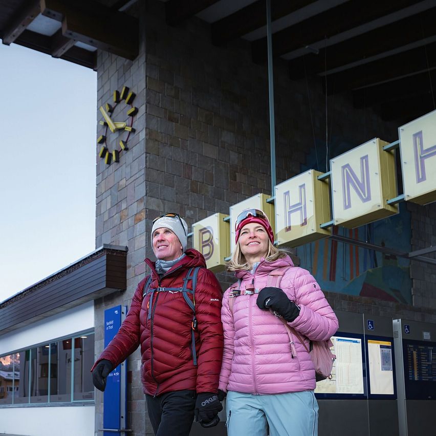 Winterwandern in der Region Seefeld_Mann und Frau kommen in Seefeld aus dem Bahnhof_Nahaufnahme