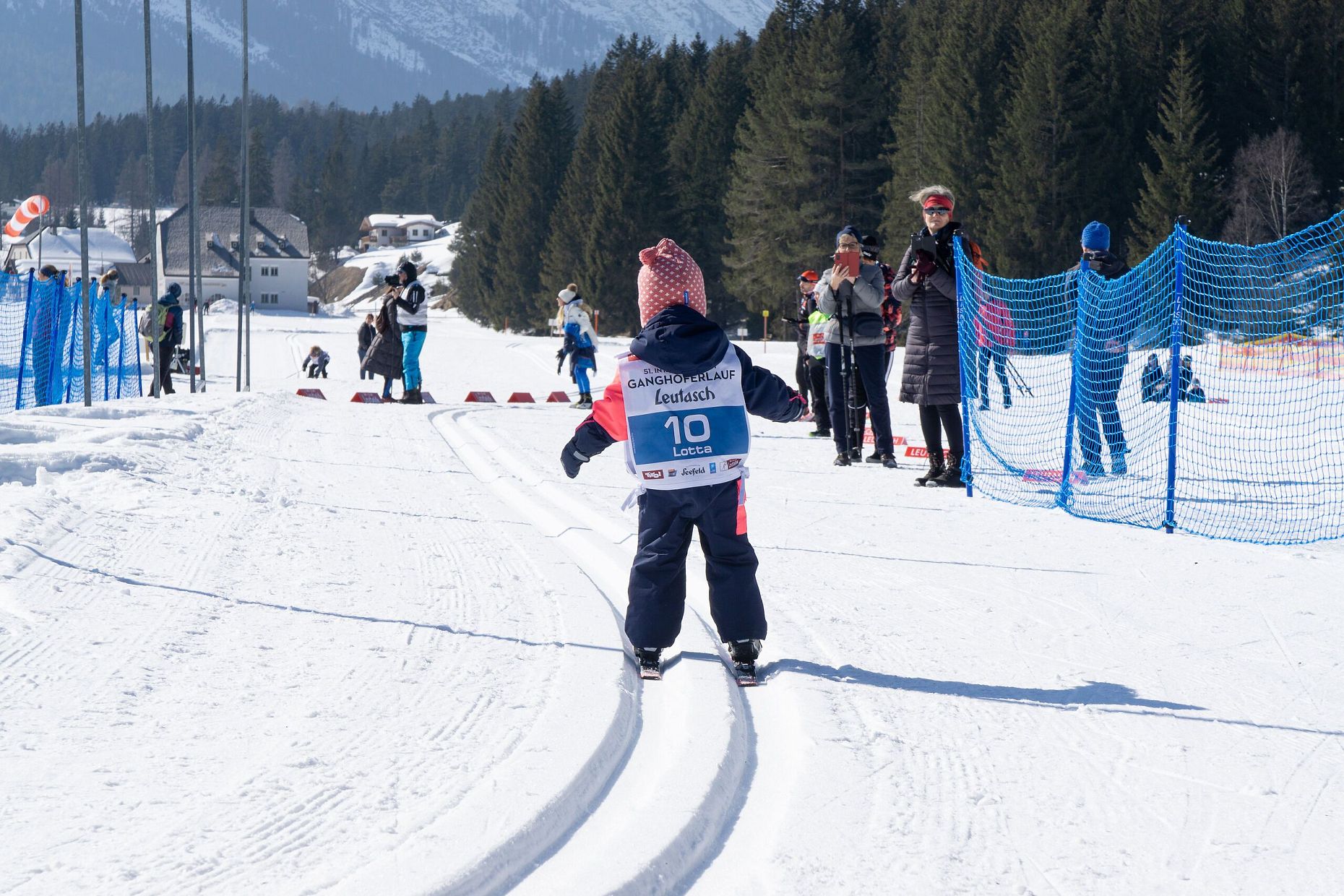 Kind auf Langlaufskiern bei Rennen in der Region Seefeld, Zuschauer säumen die Strecke.