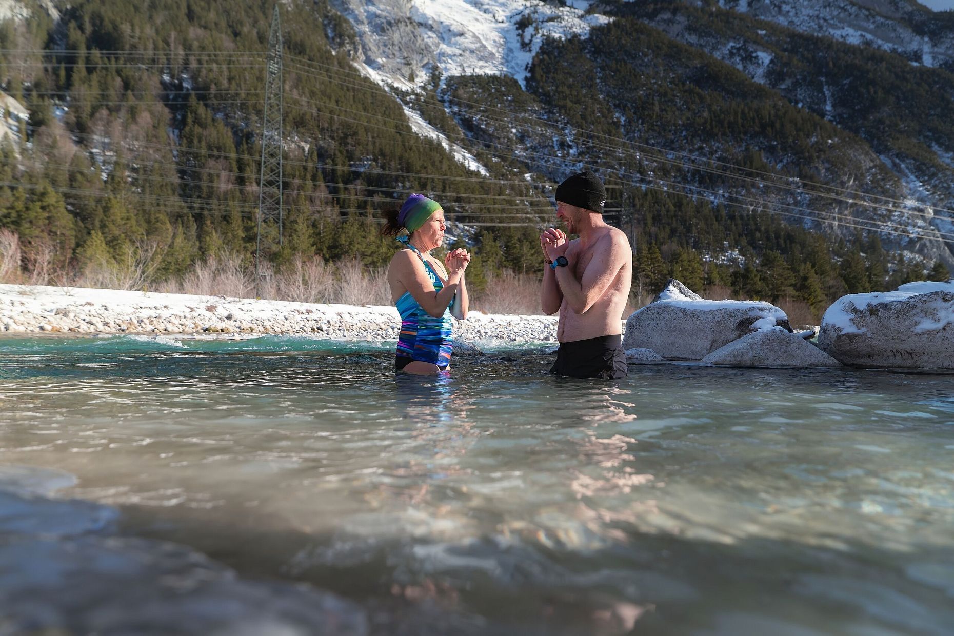 A man and a woman in a hot spring with snow-covered mountains in the background.