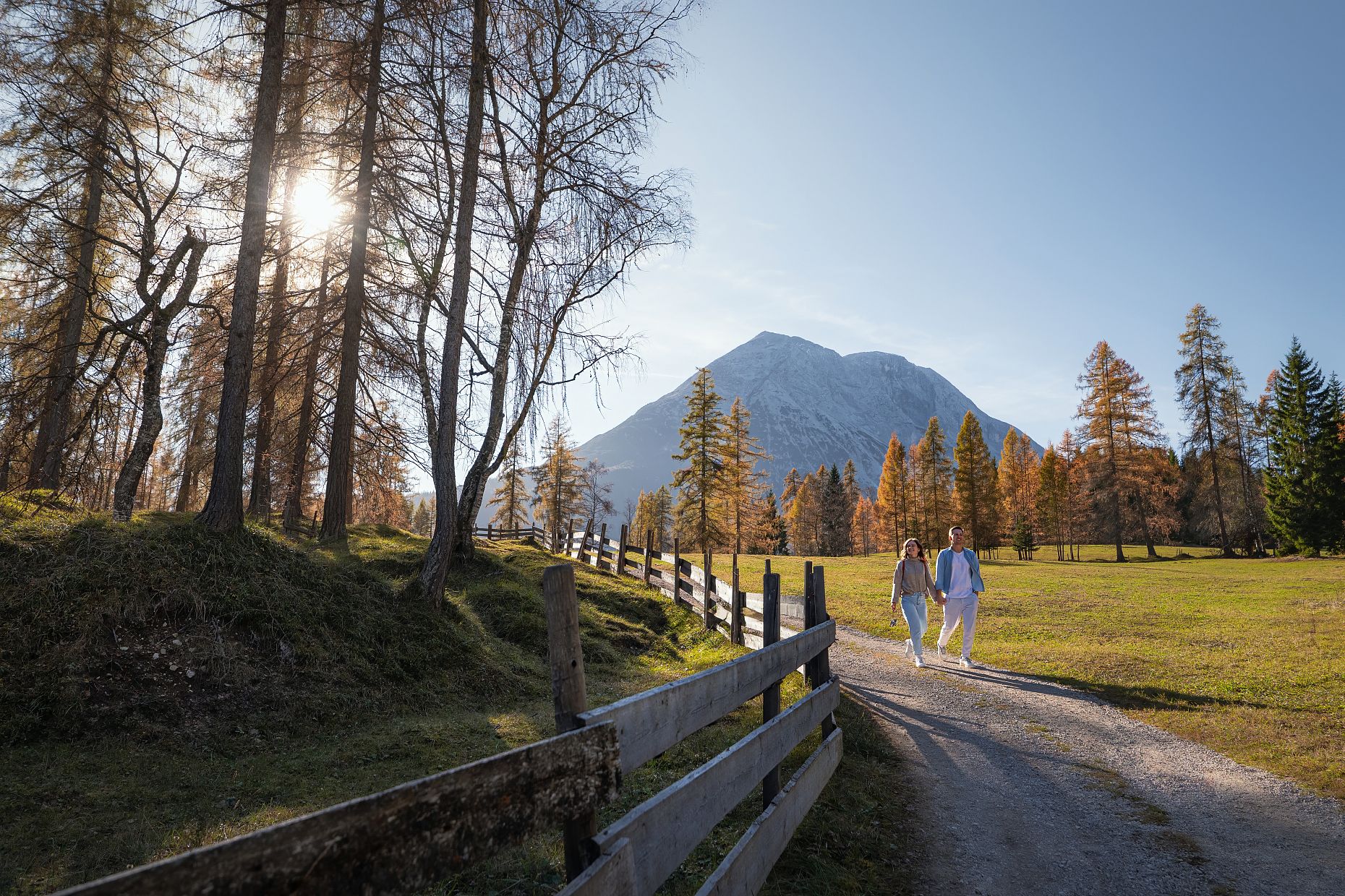 Herbstwanderung am Oberen Wiesenweg_junges Paar läuft auf breitem Weg_Hohe Munde im Hintergrund