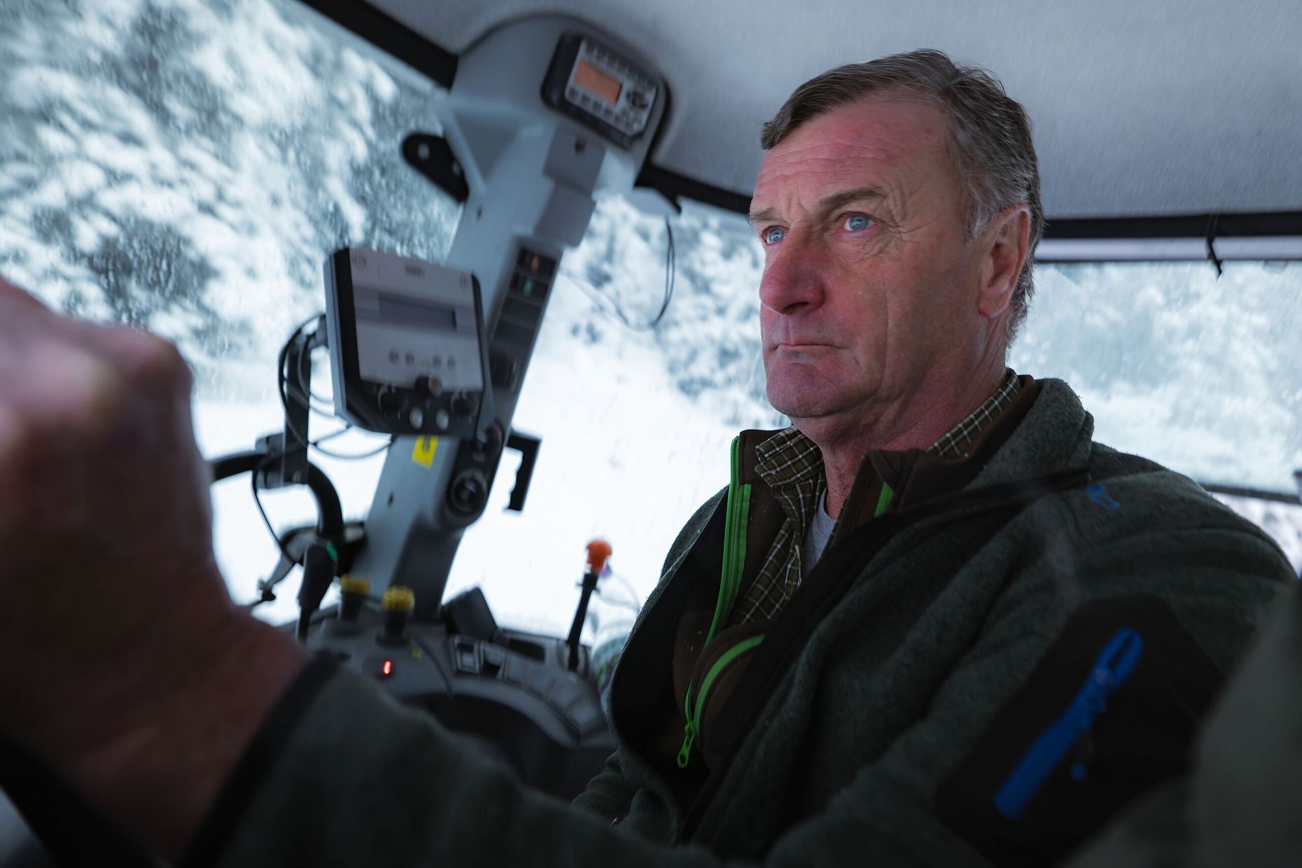 Mann fährt Schneeraupe durch verschneite Landschaft, konzentriert am Steuer.