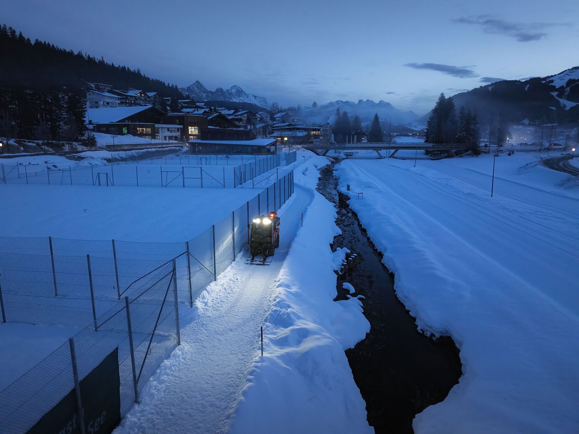 Winterlandschaft in der Region Seefeld mit beleuchtetem Traktor auf verschneitem Weg bei Dämmerung.