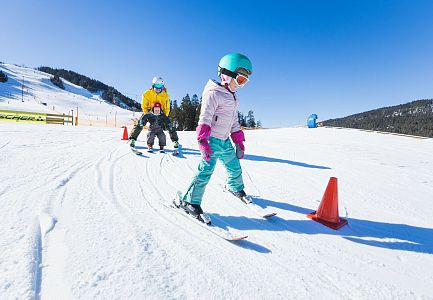 Ein kleines Mädchen skiert auf einer Skipiste, während andere Skifahrer im Hintergrund sind.