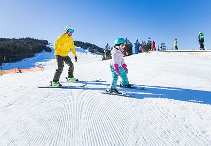 Kind und Erwachsener auf der Skipiste in der Region Seefeld, beide in bunter Skikleidung.