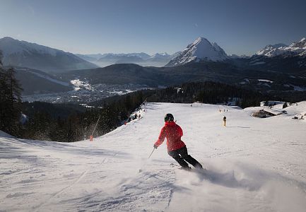 Skifahrer fährt Piste in der Region Seefeld hinunter, Alpen im Hintergrund.