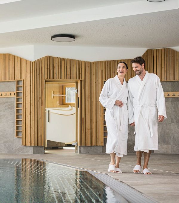 A couple in white bathrobes walking by a pool in a spa environment.
