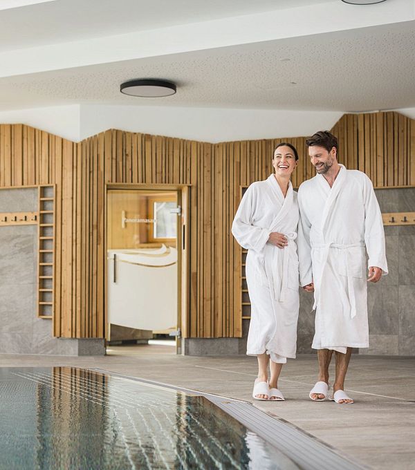 Paar in Bademänteln am Rand eines Pools in einem Wellnessbereich.