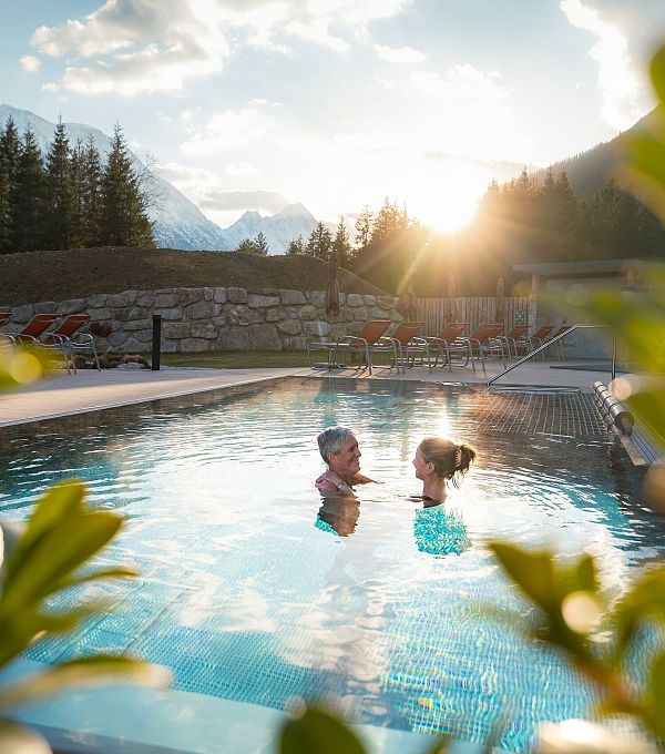 Alpenbad Leutasch im Frühling_Paar im Outdoor-Pool bei Sonnenuntergangsstimmung_Blick durch Busch