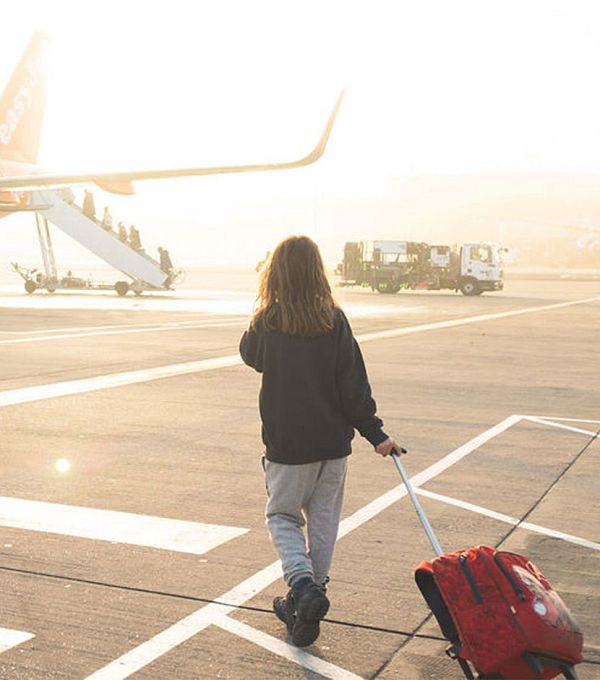 Eine Person zieht einen Koffer auf einem Flughafen, im Hintergrund steht ein easyJet Flugzeug.