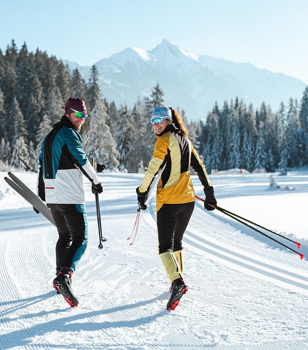 Zwei Langläufer auf einer präparierten Spur in der Region Seefeld, umgeben von verschneiten Bäumen und Bergen.