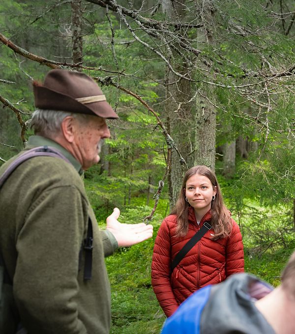 Gruppe beim Wandern in der Region Seefeld; ein Mann mit Hut spricht, umgeben von dichtem Wald.