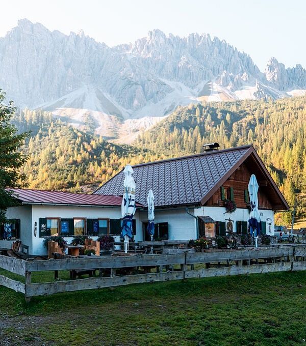 Berghütte mit rotem Dach, umgeben von Natur und Bergen.