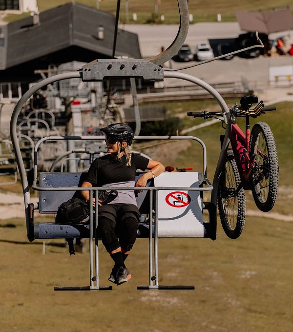 Ein Mountainbiker sitzt in einem Sessellift mit einem Fahrrad neben ihm.